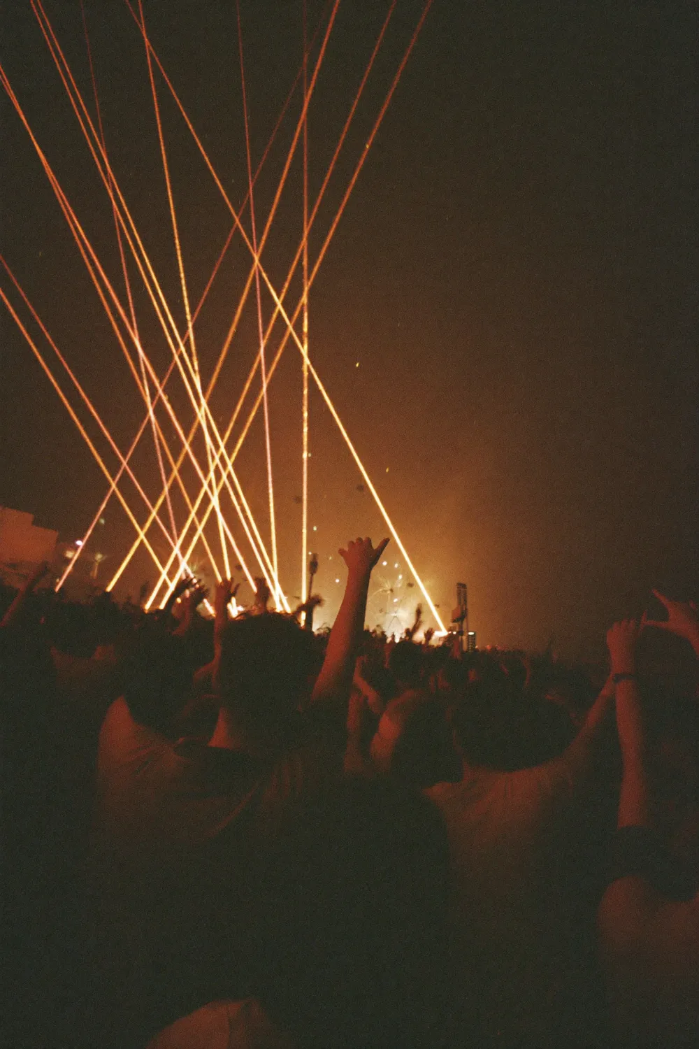 A festival crowd with hands raised under laser beams