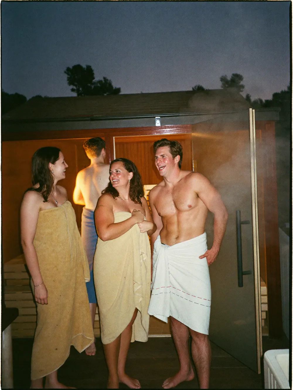 Friends in towels outside a sauna at dusk